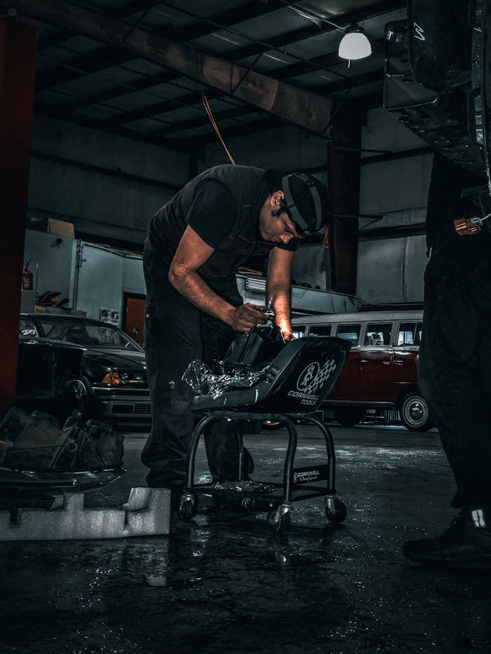 Services A mechanic focused on a car part repair in a dimly lit auto body shop.